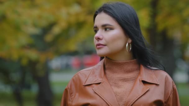 Retrato feminino close-up jovem confiante bem sucedido sério empresária vira olha para a câmera atraente hispânico mulher morena em pé no outono parque pensativo milenar senhora modelo posando ao ar livre — Vídeo de Stock