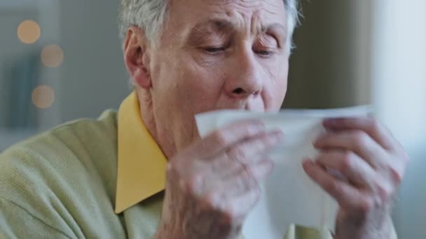 Old Caucasian 60s man sick suffering aged mature senior ill 70s male patient grandfather sneezes runny nose wipes snot with paper tissue seasonal allergy symptoms disease respiratory infection at home — Stock Video