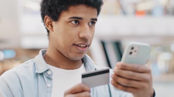 Африканський домініканець 20 чоловік тримає телефон і кредитну картку успішною онлайн-покупкою бронювання електронних транзакцій за допомогою віртуальних грошей онлайн-покупок за допомогою мобільного додатка перевірка банківських рахунків — стокове відео