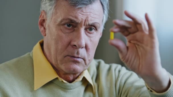 Unhealthy old senior retired male Caucasian sick ill patient 60s grandfather man holds pill with medicine painkiller cardiological drug cure from disease. Portrait aged 70s pensioner holding capsule — Video Stock