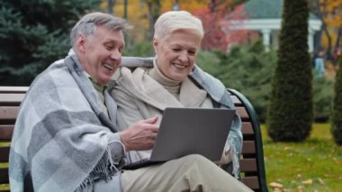 Older happy caucasian husband wife mature elderly couple grandparents family look at screen laptop work remotely browser good news watch funny video on internet choose make online purchases shopping