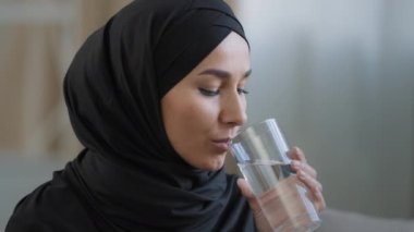 Türbanlı mükemmel cilde sahip Arap genç bir kadın. Bir bardak temiz filtrelenmiş su içiyor. Güzel bir kız ferahlatıcı mineral sıvı hidratlaştırıcı susuzluk çekiyor.