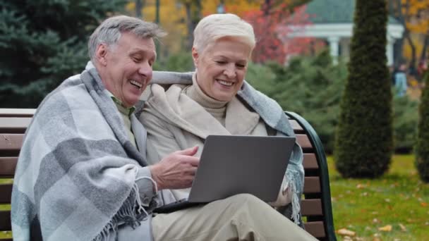 Older happy caucasian husband wife mature elderly couple grandparents family look at screen laptop work remotely browser good news watch funny video on internet choose make online purchases shopping — Wideo stockowe