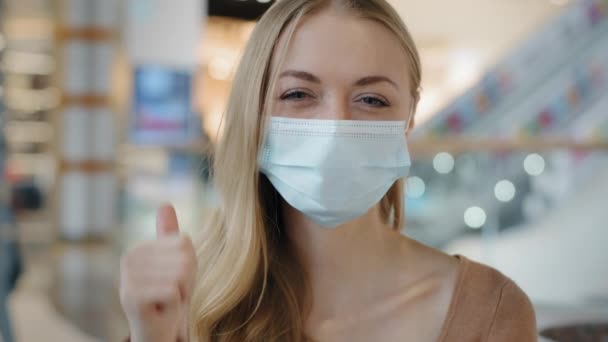 Indoors portrait caucasian woman patient girl female lady in face protective medical mask protecting health from coronavirus infection covid shows like puts thumbs up recommends wearing respirator — стоковое видео