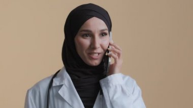 Arap Müslüman genç cerrah kadın pratisyen doktor cep telefonuyla geleneksel tesettürlü tesettüre giriyor hasta uzaktan kumandalı kadın İslami terapist klinikte tedavi amaçlı mobil konuşmaları tartışıyor