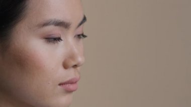 Yan görünüş, çekici, Asyalı bir kadının yüzünü kapamak, üzgün bir şekilde stüdyoda ciddi bir Koreli kızı üzmek. Japon Çinli kadın uzaktaki portreye bakıyor. Gözlerin iyi görüyor. Mükemmel cilt kozmetolojisi
