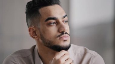 Pondering serious young arabian man businessman male student sit at home office hold hand on chin lost in thoughts dreamy looking away consider market risks make difficult decision generate new ideas
