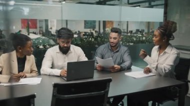 Motive olmuş Afrikalı kadın takım lideri şirket geliştirme stratejisini açıkladı. Ofisteki çeşitli meslektaşlar şirket eğitiminde çok ırklı işçilerin birlikte çalıştığı belgeleri tartıştı.