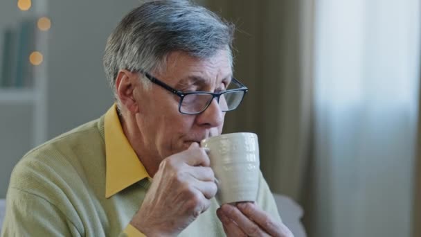 Blanke eenzame ziekelijke oude bejaarde man jaren '60 man jaren' 70 grootvader drinken hete thee vloeibare antipyretische geneeskunde denken over probleem ontspannen thuis zitten op de bank eenzaamheid ziek gepensioneerde — Stockvideo