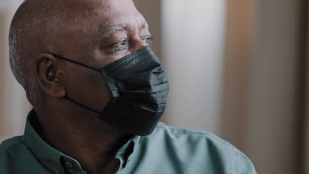 Портрет старого самотнього африканського домініканця 60-х років дідуся зрілого старшого чоловіка сумного пацієнта-пенсіонера в чорній медичній масці вдома, який дивиться в приміщенні, думаючи про ізоляцію ковалентної пандемії коронавірусу — стокове відео