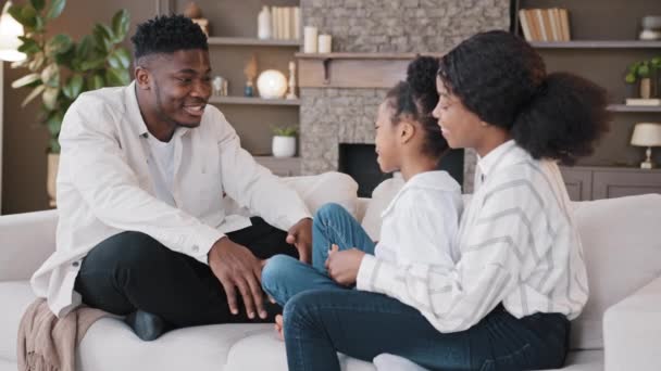 African family adult parents and schoolgirl daughter girl child sitting on sofa at home in living room casual communication talking conversation to each other spend time together in own apartment — Stock Video