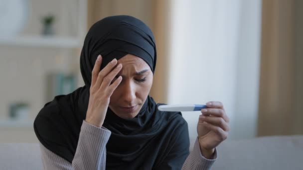 Shocked unhappy islamic young woman arabian muslim girl in hijab female adult pregnant feeling fear looking at positive pregnancy test result sit at home worrying about unwanted children bad reaction — 图库视频影像