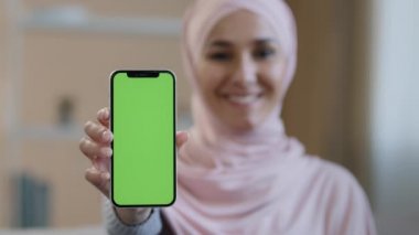 Portre gülümseyen Arap Lübnanlı Müslüman kız tesettürlü kadın tesettürlü akıllı telefonu ön gösterim cep telefonunda yeşil ekranlı kamera reklamında uygulama servisi dijital cihaz reklamı