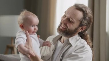 Yakın plan mutlu baba şefkatli orta yaşlı baba sakallı adam küçük kızı tutuyor çocuk zıplıyor erkek ebeveyn gülerek evde bebek bakıcılığı yapan yeni doğmuş bebekle vakit geçiriyor.