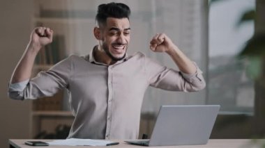 Young successful joyful hispanic man male investor businessman hold document look at laptop win online lottery celebrate victory get new distance job opportunity rejoice read good news feel motivation