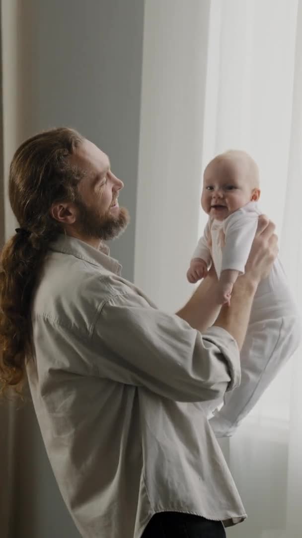 Verticaal uitzicht Kaukasische volwassen vader liefdevolle zorgzame papa houden baby dochter weinig zoon gooien in de lucht schudden verhoogt dansen met zuigeling thuis hebben plezier met pasgeboren vliegen spelen spel leuk teder — Stockvideo