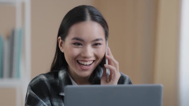 Happy smiling Asian girl Korean female freelancer chatting with friends on phone answering call friendly looking at laptop screen remote working business negotiation making online order by smartphone — 비디오