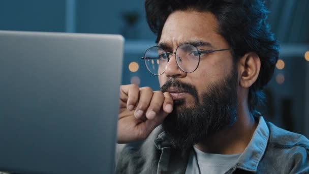 Ориентированный арабский индийский бородатый мужчина фрилансер в очках, работающий дома за компьютером поздно вечером, глядя в экран поискового решения чувствует сомнение создание онлайн-проекта мышления о решении проблемы — стоковое видео