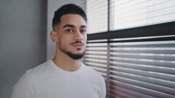Millennial 30s árabe hispano indio masculino morena barbudo hombre en camiseta blanca de pie cerca de persianas ventana en casa por la mañana mirando a la cámara sonriente dientes dentales salud odontología servicio — Vídeos de Stock