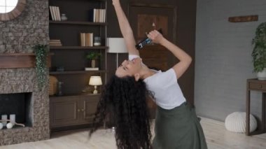 Genç ve aktif bir kadın modern oturma odasında dinamik dans eder. Müzik dinler. Uzaktan kumandayı kullanır.