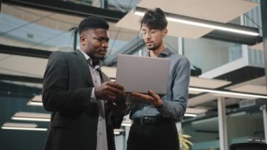 Çok ırklı iş ortakları ofiste duruyor Afrikalı bankacı erkek yönetici Arap iş adamı analizcisiyle online başlangıç projesi yararını tartışıyor dizüstü bilgisayar takım çalışması pazarlığı sunumunu gösteriyor