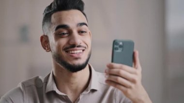 Mutlu genç Arap erkek iş adamı, akıllı telefon konuşması video görüşmesiyle yapılıyor. Sanal görüşme için arkadaşınızla sohbet edin. İyi haberleri paylaşın. Sosyal uygulama mesafesi iletişimini kullanın.