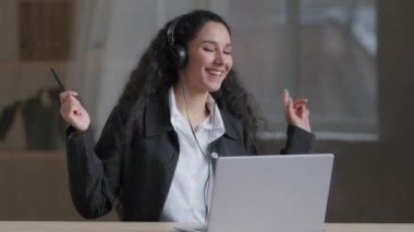 Mutlu, genç, Arap kız, kaygısız öğrenci kulaklık takıyor. Müzik dinliyor, enerjik hareketler yapıyor. Yüksek kaliteli şarkılar söylüyor.