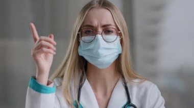 Tıbbi maskeli kadın doktor kameraya bakıyor kızgın işaret parmağı yok olumsuz jest yok beyaz önlüklü psikolog kadın hemşire elle agresif bir açıklama yapıyor.