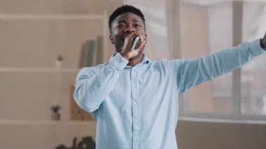 Mutlu Afro-Amerikan iş adamı enerjik müzik dinle favori şarkıları söyle cep telefonu görüntülü akıllı telefon iş günü dans ederken mikrofon rahatlaması gibi hareket eden karaoke yarışması