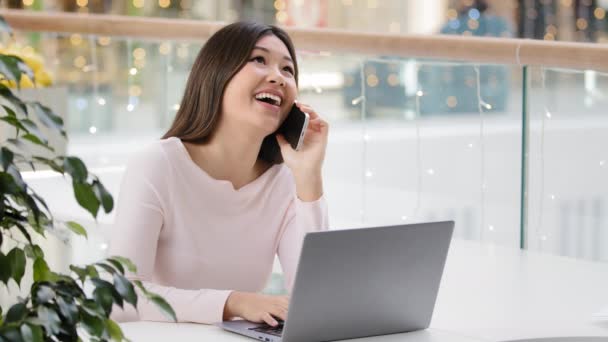 Happy Asian Korean woman freelancer student businesswoman holding mobile phone call working with laptop multitasking girl making online order communicating with friend distant friendly carefree talk — Stockvideo