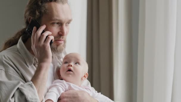 Cheerful carefree middle-aged caucasian man bearded father answering call talking to wife mom with phone online order booking baby food holding little daughter newborn infant at home chatting friendly — Vídeo de stock