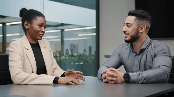 Hombre de negocios árabe y mujer de negocios africana hablando en la mesa de oficina. Dos socios gerente femenino y jefe masculino negociando en compañía. Colegas mujeres y hombres trabajadores discutiendo proyecto corporativo — Vídeo de stock