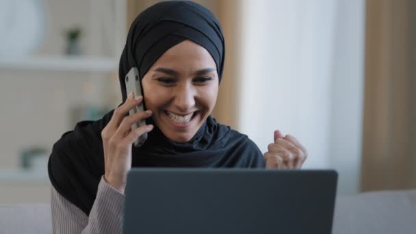 Happy smiling arabian woman muslim girl in hijab female freelancer talking by mobile phone with friend answering call enjoy good news has business negotiation use laptop online victory successful deal — Vídeo de Stock