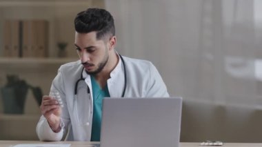 Genç Arap erkek doktor hemşire, profesyonel pratisyen. Laptop üzerinde çalışıyor. Tıbbi uygulama kullanıyor. İlaç reçetesi okuyor.