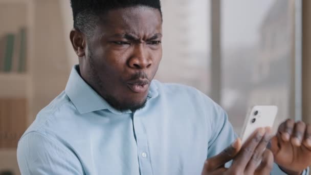Afrikanische männlich überrascht millennial 30s Mann Arbeiter sprechen Fernbedienung auf Handy schönen amerikanischen erwachsenen Kerl machen Videoanruf schockiert durch plötzliche angenehme virtuelle Verbindung mit Freund sagen wow — Stockvideo
