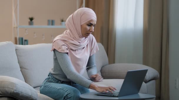 Mladý islámský arabský obchod žena muslimský dívka v hidžábu sedí na pohovce pomocí notebooku doma pracuje studovat online pocit stresu bolesti břicha špatný boj trpí bolestí břicha má zažívací potíže — Stock video