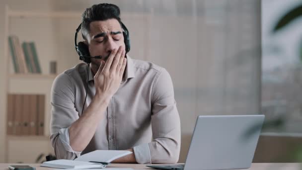 Uttråkad latinamerikan arbetare trött manlig agent bära headset titta på bärbar dator gör företag konferens internet video samtal omotiverad anställd ointresserad av tråkig avlägsen arbete känner brist på motivation gäspning — Stockvideo