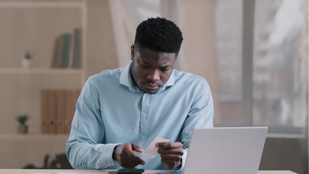 Young African focused man bank employee bookkeeper hold payment bill manage personal budget use calculator calculates expenses costs credit balance keeps accounting savings sitting at home office desk — Stock Video