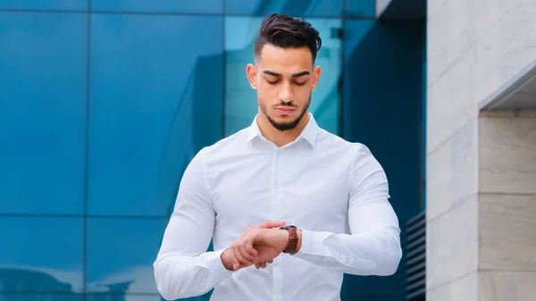 Portrait serious upset angry hispanic man bearded guy disgruntled businessman boss wears formal stylish shirt stands outdoors looking at wrist watch worried about being late lateness time rush waiting — Stock Photo, Image