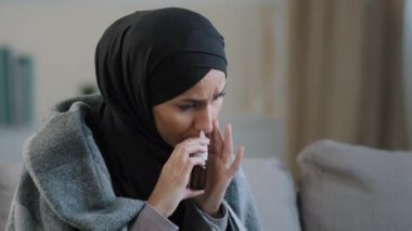 Müslüman Arap kadın hasta tesettürlü İslamcı kız evde rahat bir kanepeye oturur burun akıntısını tedavi eder burun spreyi kullanır burun spreyi tedavisini her gün tedavi eder mevsimsel alerji semptomlarını düzeltir.