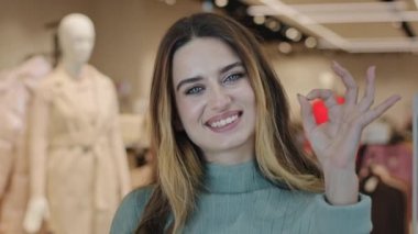 Portre genç beyaz kadın müşteri alıcı genç tüketici kız alışveriş merkezindeki giyim mağazasında dikilip kameraya bakarken her şey yolunda görünüyor.