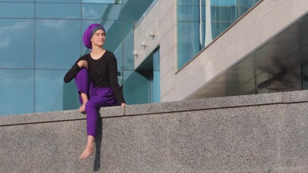 Lugn ung muslim flicka buddist i hijab ensam dam kvinna vacker kvinna sitter på byggnad stad skyskrapa bakgrund ser runt väntar drömmande tänkande överväger vila njuter av utsikten — Stockvideo