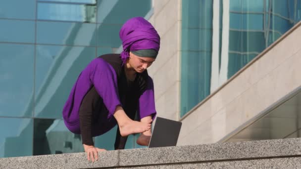 Vicces erős tornász akrobata nő diák lány muszlim hölgy hidzsáb áll kéznél gépelés lábakkal laptop a város épületében háttér dolgozik tanul online üzleti jóga asana póz — Stock videók