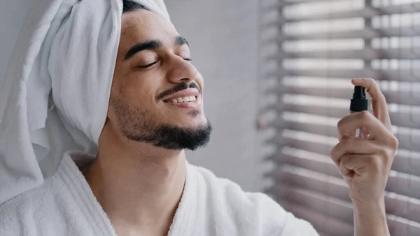 Смешной латиноамериканец бородатый индиец с белым полотенцем для ванны на голове в ванной косметические процедуры идеальный уход за кожей мужчины с помощью увлажняющего брызг лица природный здоровый косметический увлажняющий лицо — стоковое фото