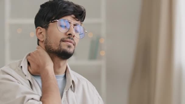 Retrato jovem cansado árabe indiano estudante homem de negócios barbudo cara com óculos sentado em casa no escritório no sofá sente desconforto dor no pescoço sofre de dor danos à postura desconfortável — Vídeo de Stock