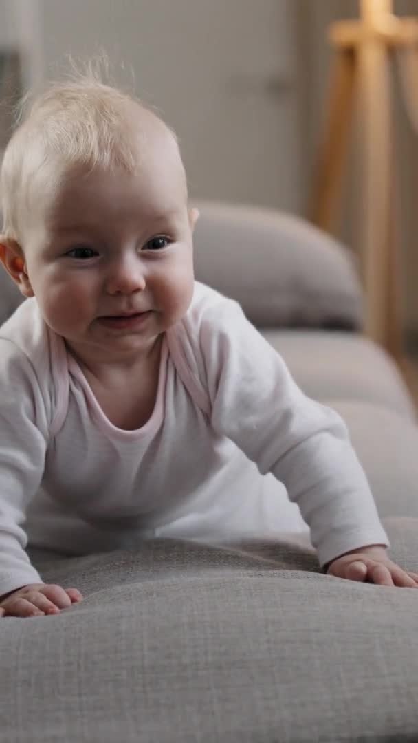 Vista vertical feliz bonito pequeno bebê menina menino recém-nascido órfão rasteja no quarto no sofá. Criança brinca em casa sorrindo rir aprende rapidamente rastejando no sofá criança explorando casa curioso — Vídeo de Stock