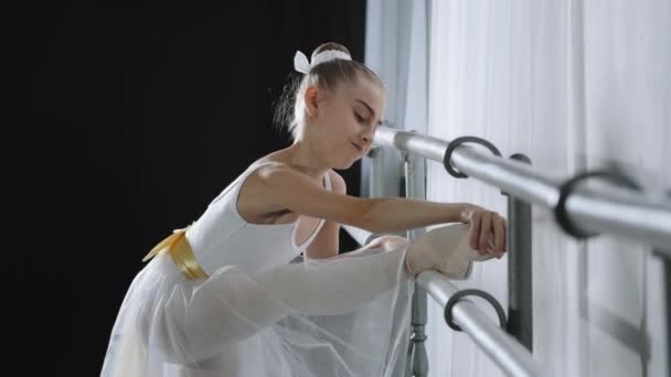 Güçlü, esnek, esnek bir genç kızın bale çubuğuyla esnemesi. Bacak kaslarını esneten beyaz etekli kız çocuk balerin dans okulunda koreografi egzersizi yapıyor. — Stok video