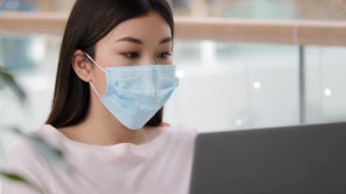 Asian student Korean business woman in medical face mask freelancer writer journalist typing working laptop using free Wi-Fi studying with computer app e-learning distant education pandemic e-commerce