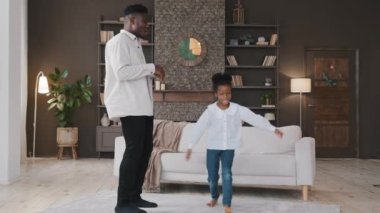 Mutlu iki aktif Afro-Amerikan ailesi oturma odasında dans ediyor, kaygısız yetişkin baba ve tatlı kız çocuk kız eğleniyor ev disko partisinde birlikte müzik dinleyip eğleniyorlar.