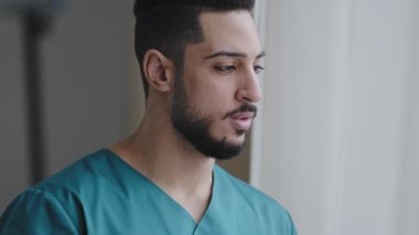 Genç, düşünceli İspanyol doktor erkek, düşünceli Arap hemşire, pratisyen doktor hastane işyerindeki pencerenin yanında dur ve hasta ziyaretini bekle üzgün doktor, karantinaya son vermeyi düşün.